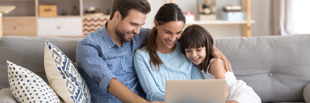 Couple and little daughter sit on sofa using pc