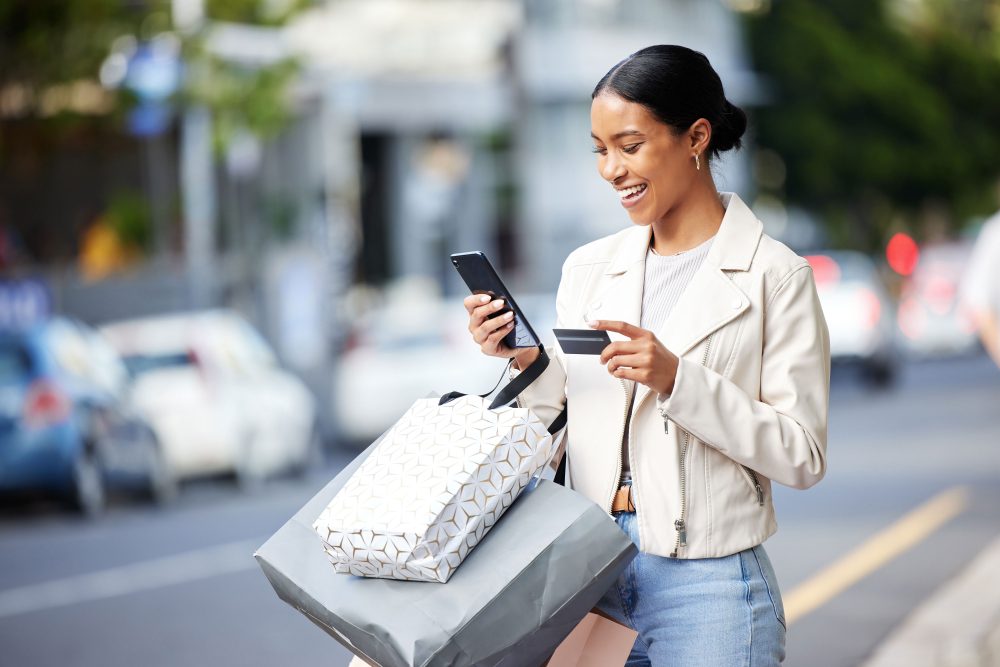 Happy woman with her phone, credit card and bag after shopping in the city