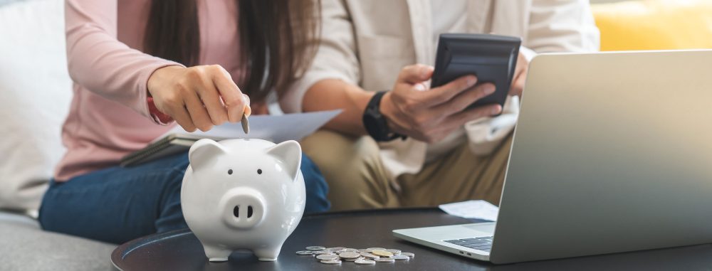A happy young couple puts a coin in piggy bank to save money