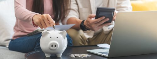 A happy young couple puts a coin in piggy bank to save money