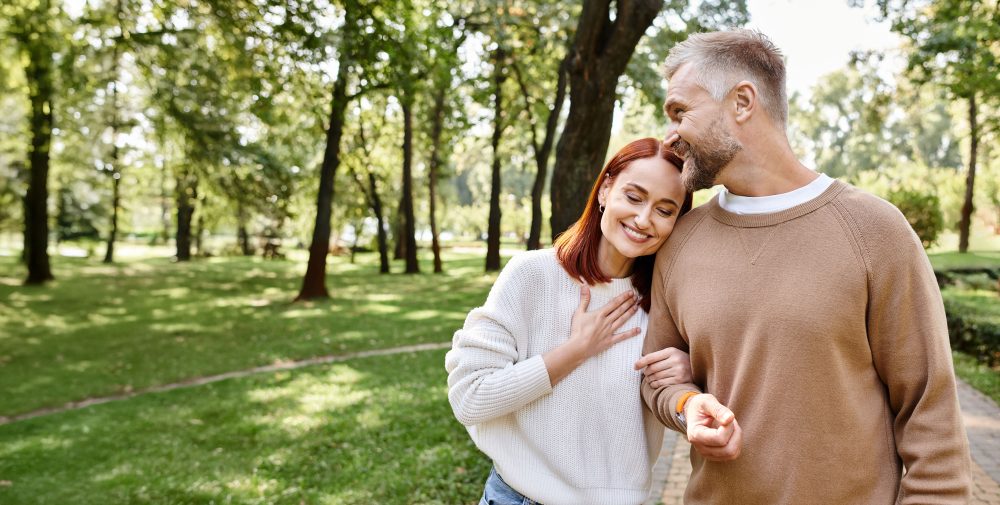 Adult man and woman in casual clothing walking peacefully through a park.