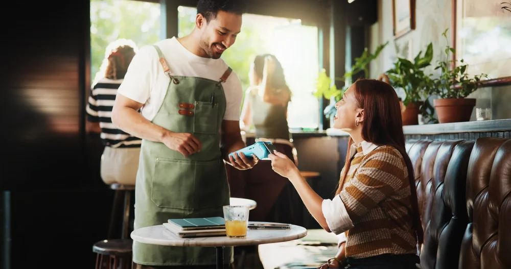 Happy people, customer and waiter with pos machine in coffee shop for credit card payment.